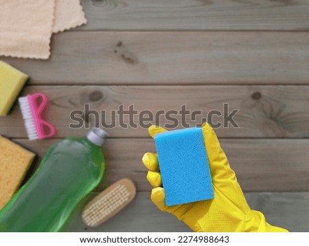 Kitchen sponge in hand. Flat lay. Concept of spring Deep clean of house. Place for text.  Rubber glove with washcloth on blurred background of wooden table with cleaning tools. Copy space. Top view. Royalty-Free Stock Photo #2274988643