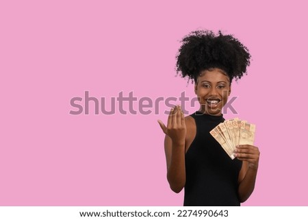 woman smiling holding brazilian money bills, positively surprised, space for text, person, advertising concept on pink background
