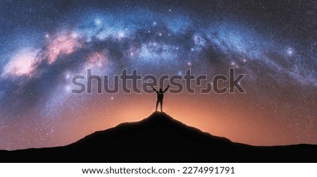 Milky Way and happy man on mountain peak at starry night. Silhouette of guy with raised up arm on the hill, sky with stars, yellow light in Nepal. Galaxy. Space landscape with milky way arch Royalty-Free Stock Photo #2274991791
