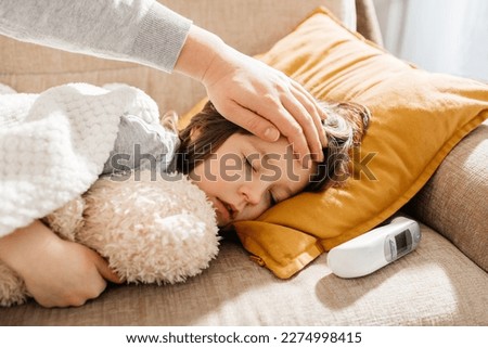 A parent checks the temperature of a sleeping child with his hand. The sick boy sleeps on the couch in the living room. Sick children Royalty-Free Stock Photo #2274998415