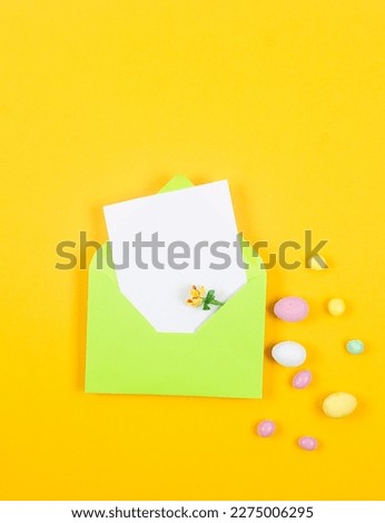Easter Colorful candy chocolate eggs and light green envelope with blank card on yellow background. Easter holiday and tradition concept. Preparation for holiday. 