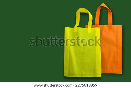 two yellow and orange polypropylene tote bags with copy space for text. eco-friendly recycled spunbond bags on dark green background