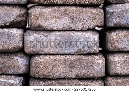 Close up macro photograph of a pile of recycled red or brown weathered concrete masonry pavers with rounded corners and chipped edges sitting in vertical stacks.