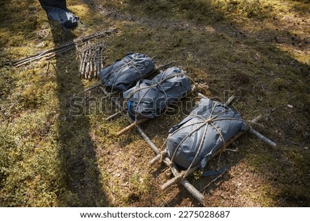 Makeshift stretchers made of small logs and tarpaulins, tied together with a rope, lie on the ground in the forest. Preparing for a hike in the wild. Royalty-Free Stock Photo #2275028687