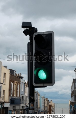 Green traffic light on an urban street with buildings behind and a cloudy sky