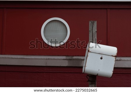 Selective focus outdoor exterior at white post box in front of red boat house wall and circle window.