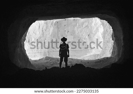 Silhouette of man standing in opening of cave