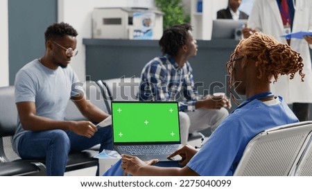 African american nurse looking at laptop with greenscreen, analyzing chroma key display in waiting room. Specialist working with blank mockup template and isolated copyspace, health care.