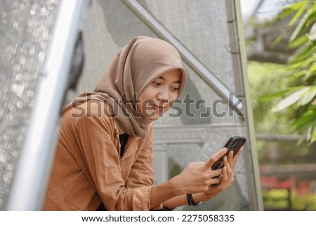 Asian woman wearing modern hijab playing social media using her smartphone in the park