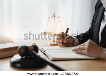 Asian female lawyer or legal advisor working on the scale of justice sitting at her desk and holding a pen to look at the information Detailed content about the scale of jurisprudence to study. Royalty-Free Stock Photo #2275072729
