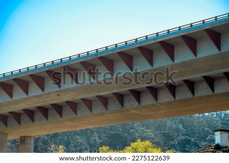 Freeway or highway overpass in suburban area of california with red accent design metal plates triangular with urban trees. House i background in foresty suburban neighborhood with hazy white sky.