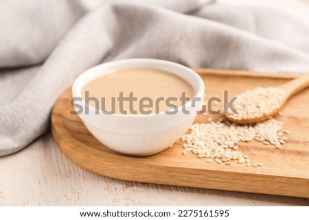 Board with bowl of tasty tahini and sesame seeds on light wooden table, closeup Royalty-Free Stock Photo #2275161595
