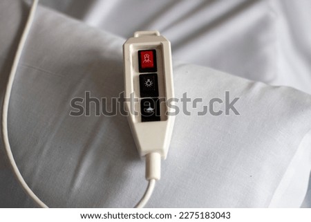 Hospital call control with a red emergency button resting on a bed with white sheets Royalty-Free Stock Photo #2275183043