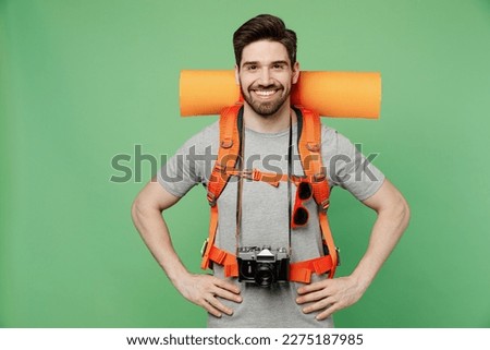 Young traveler white man carry backpack stuff mat hold photo camera isolated on plain green background. Tourist leads active healthy lifestyle walk on spare time. Hiking trek rest travel trip concept