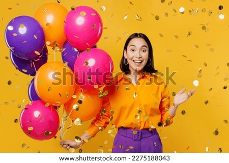 Happy fun young surprised fun woman wearing casual clothes celebrating near balloons in confetti glitters rainfall spread hand isolated on plain yellow background. Birthday 8 14 holiday party concept Royalty-Free Stock Photo #2275188043