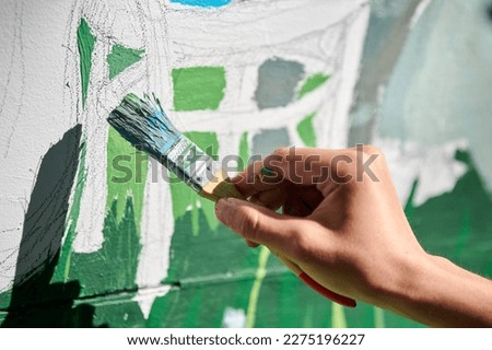Girl artist hand holds paint brush and draws green nature landscape on white canvas at outdoor art painting festival, paintings art picture process. Woman artist paints atmospheric surreal picture Royalty-Free Stock Photo #2275196227