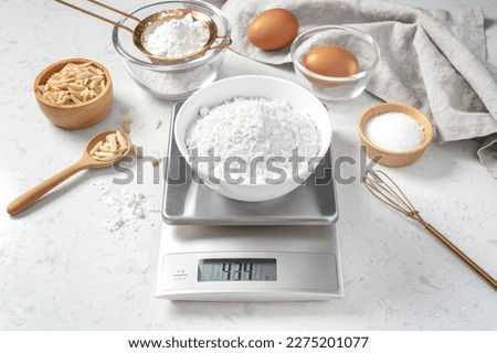 Flour in white bowl measuring on digital scale with cake or bakery ingredients and utensil on marble kitchen table Royalty-Free Stock Photo #2275201077