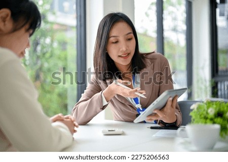 Beautiful and focused millennial Asian businesswoman using tablet, discussing work and working with her colleague in the office. Royalty-Free Stock Photo #2275206563