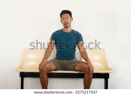 An Asian man sitting on a bench looking bored Royalty-Free Stock Photo #2275217437