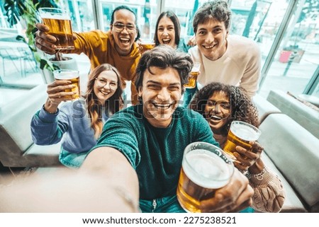 Happy friends taking selfie picture at brewery pub restaurant - Group of multiracial people enjoying happy hour drinking beer sitting at bar table - Life style concept with guys and girls hanging out