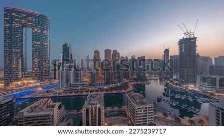 Dubai Marina panorama with boats and yachts parked in harbor and illuminated skyscrapers around canal aerial night to day transition  before sunrise. Towers of JBR district on a background