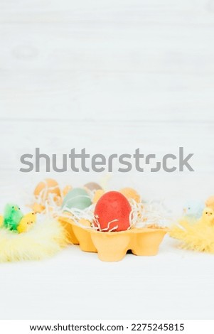 Painted multi-colored eggs in a yellow cardboard tray on a white wooden background. Easter background, symbol. Front view