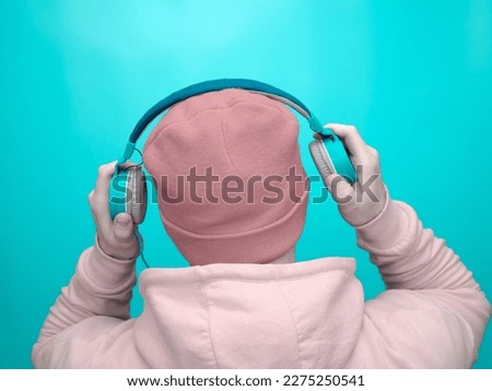 A young man in turquoise, mint musical headphones on a studio background. Happy smiling man in hoodie and headphones listening to his favorite music. Music background with stylish man.