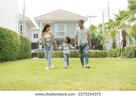 A picture of a mother and father with their little daughter standing in the outdoor garden in front of the house, laughing and playing happily.