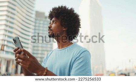 Closeup portrait of  young African American man in light blue t-shirt using his smartphone. Man looks at photos, videos in his mobile phone. Royalty-Free Stock Photo #2275256533