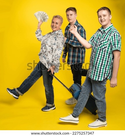 family with a suitcase. Studio colored background. blue yellow. Cheerful, plump woman and two guys, son go on vacation. lady holding money, laughing. body positivity plus size