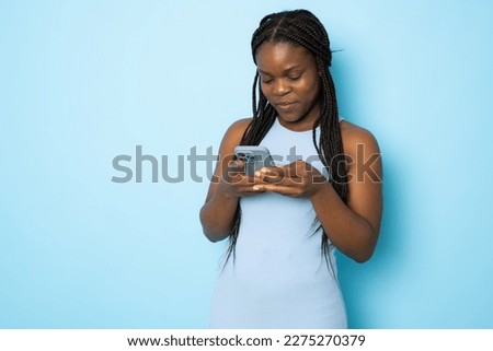 Portrait of young cheerful black lady using Smartphone For Messaging With Friends, Happy African American Lady Texting On Cellphone while standing Over blue studio background, Copy Space