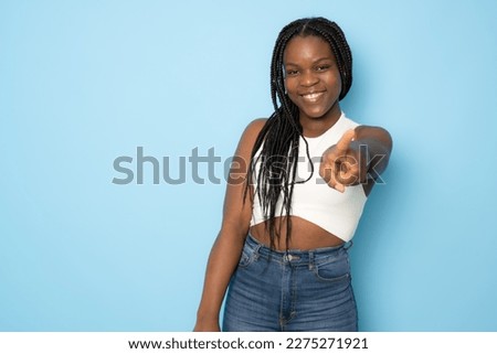 Photo of happy young african lady in casual clothing standing isolated over blue background. Looking camera while pointing to you.