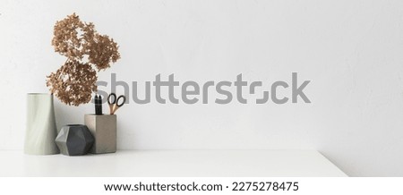 White desk, with empty space. Minimalist workspace with design supplies and decorative dried branches, flowers in a vase against white wall. 