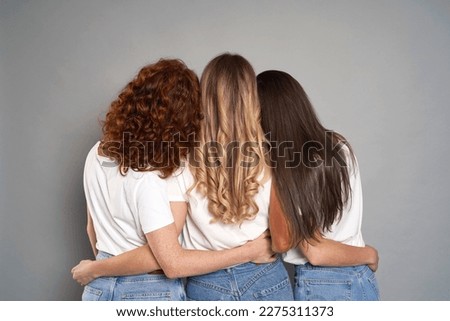 Back view of three young caucasian women wearing blue jeans and white tshirt on grey background Royalty-Free Stock Photo #2275311373