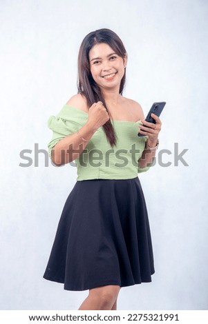 asian girl is listening to music looking at mobile phone with smile on white background. happy facial expressions, enjoying and happy