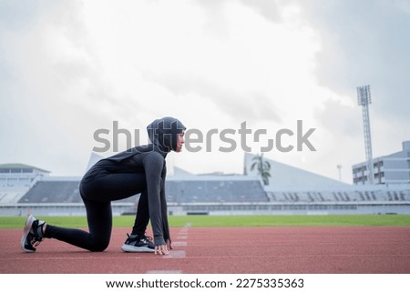 A young asian Muslim woman wearing a black hijab is exercising and running at an outdoor stadium in the morning. Modern Muslim woman concept,  Muslim woman sport concept, Islam Royalty-Free Stock Photo #2275335363