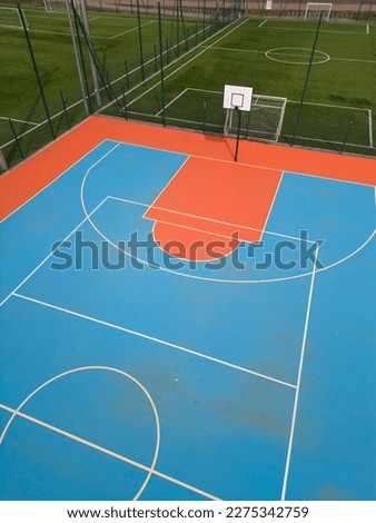 aerial view of a green football field and a colorful basketball court, providing a glimpse of two different sports facilities side by side. Royalty-Free Stock Photo #2275342759
