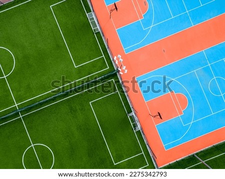 aerial view of a green football field and a colorful basketball court, providing a glimpse of two different sports facilities side by side. Royalty-Free Stock Photo #2275342793