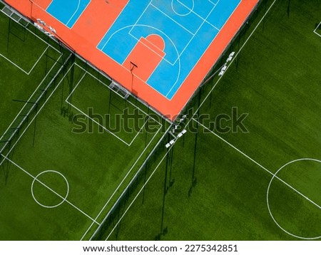 aerial view of a green football field and a colorful basketball court, providing a glimpse of two different sports facilities side by side. Royalty-Free Stock Photo #2275342851