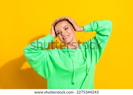 Photo of youngster hipster lady optimistic person hands touch head carefree wear green hoodie smiling have fun isolated on yellow color background