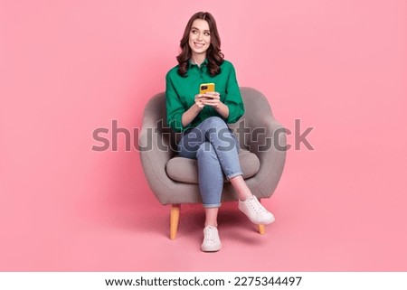 Full size photo of gorgeous cute girl dressed green shirt sit on armchair hold smartphone look empty space isolated on pink background