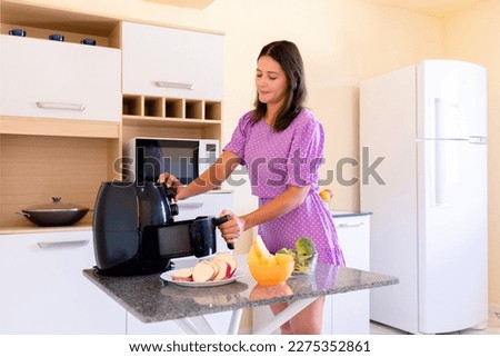 Brazilian woman using air fryer to fry food in home kitchen. Electric fryer without oil Royalty-Free Stock Photo #2275352861