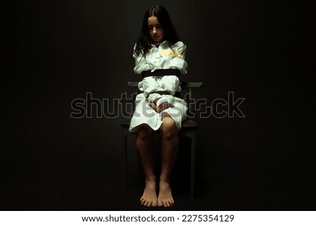 A woman in a straitjacket sitting on a black isolated background. Royalty-Free Stock Photo #2275354129