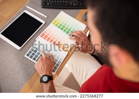 Male photo editor using graphics tablet in office, top view of unrecognizable man designer sitting at workdesk, checking color palette, digital pad with blank empty screen, mockup