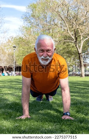 Senior man exercising, doing push ups in the park. An elderly man in good shape and health with strong arms. Vertical orientation. Royalty-Free Stock Photo #2275377515