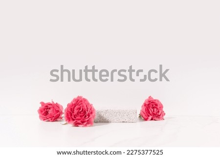 Beauty cosmetics product presentation scene made with pumice stone pedestal and pink roses on white table. Studio photography.