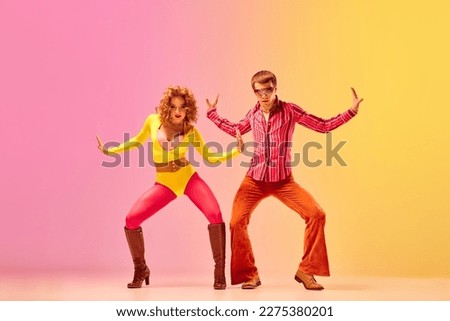 Emotions in movemets. Young stylish emotional man and woman, professional dancers in retro style clothes dancing disco dance over pink-yellow background. 1970s, 1980s fashion, music concept Royalty-Free Stock Photo #2275380201