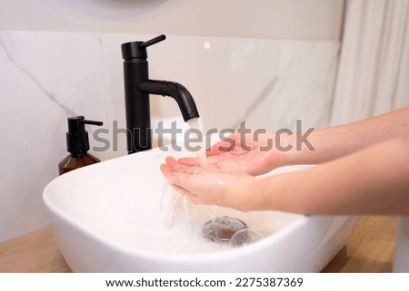 Close-up of a woman washing her hands in the bathroom to prevent a viral infection. It is recommended to wash with soap and running water. 