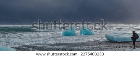 A woman photographer takes pictures of storm waves on the coast of Iceland, bringing broken pieces of ice from an iceberg.
