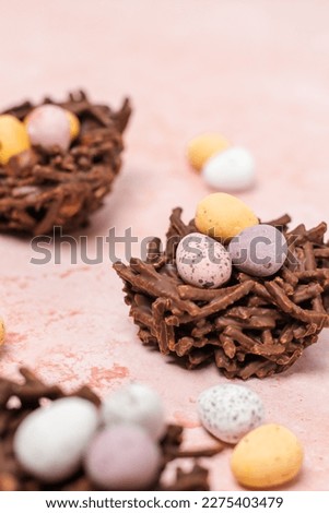 Chocolate Easter nests with mini eggs and hazelnuts. Nests are on a light pink background with mini eggs scattered around the image.  Royalty-Free Stock Photo #2275403479